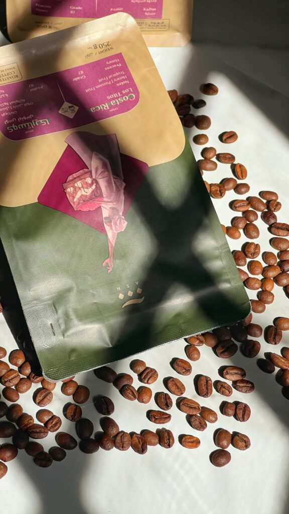 A sunlit flat lay of a coffee bag surrounded by scattered coffee beans on a white surface.